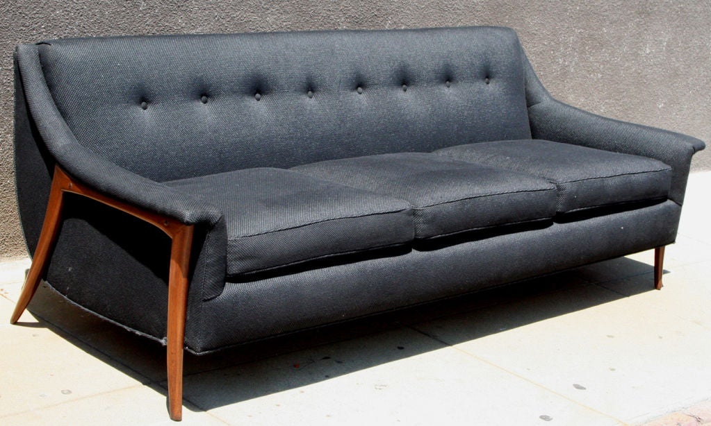 A danish modern three seat sofa with minimal exposed teak legs sculpted arm rests and tufted back in charcoal black upholstery.