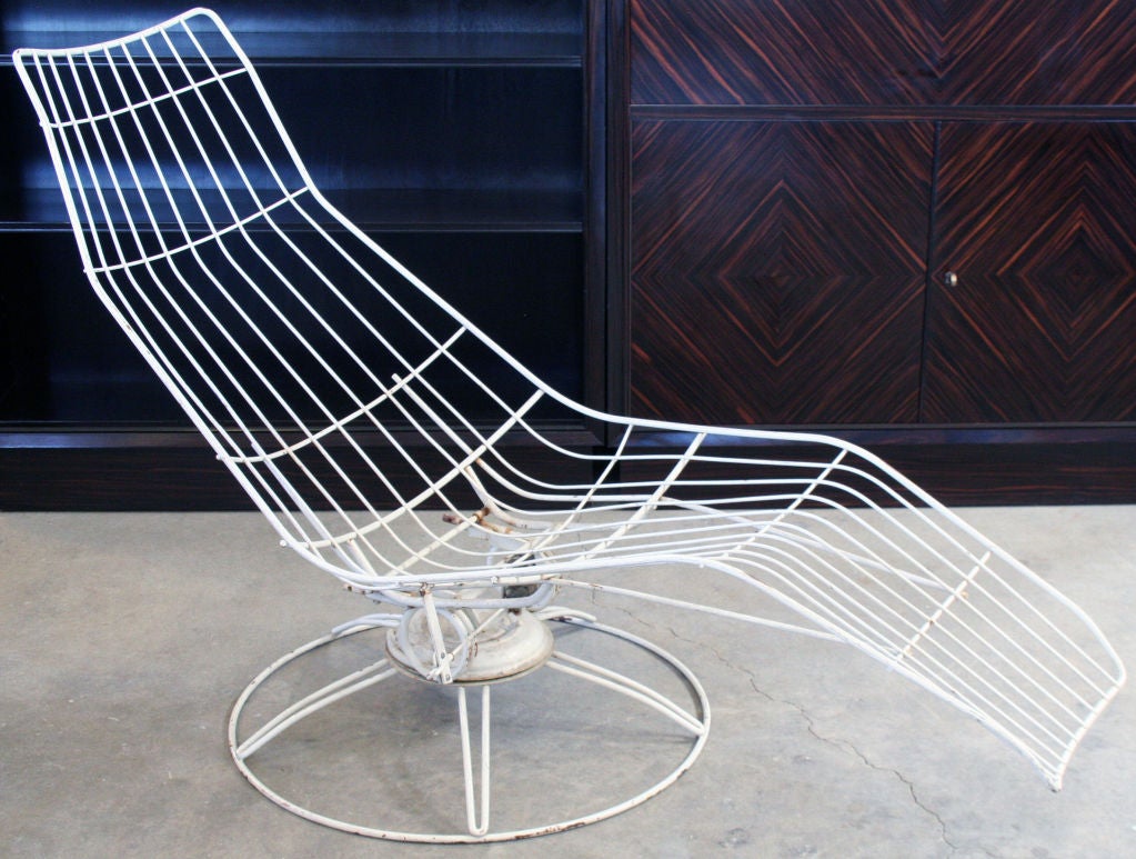A white wire framed outdoor chaise lounge on a spring steel coil tilt and swivel base. Of note is the mechanical height adjustment with a small crank to spin a set of gears which raise and lower the seat with minimal energy while seated.