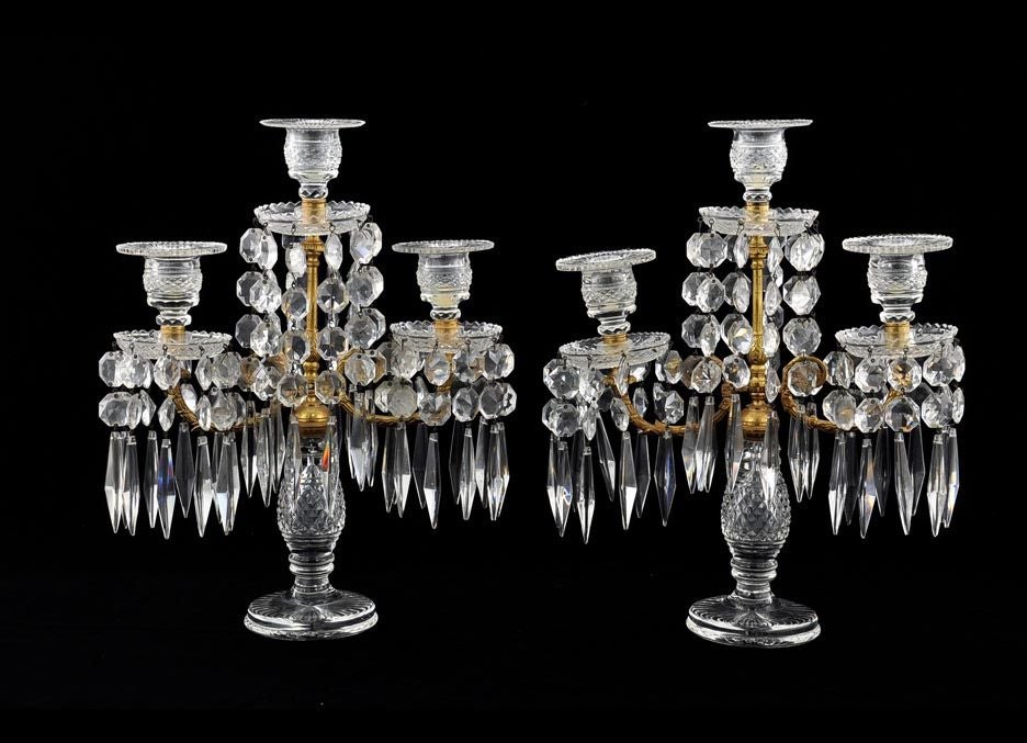 Refined PAIR Regency cut glass and brass three light table candelabra. The taller central support  with a cut glass candle cup and bobeche hung with faceted drops and flanked by a pair of  matching candle arms. All raised on a faceted baluster form