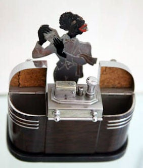 The icon of all American art deco table lighters, this 1936 beauty has a bartender with shaker behind a streamline bar with several glasses and a short stack of coasters on top.  The bar has cigarette storage on the left and right and in the center,