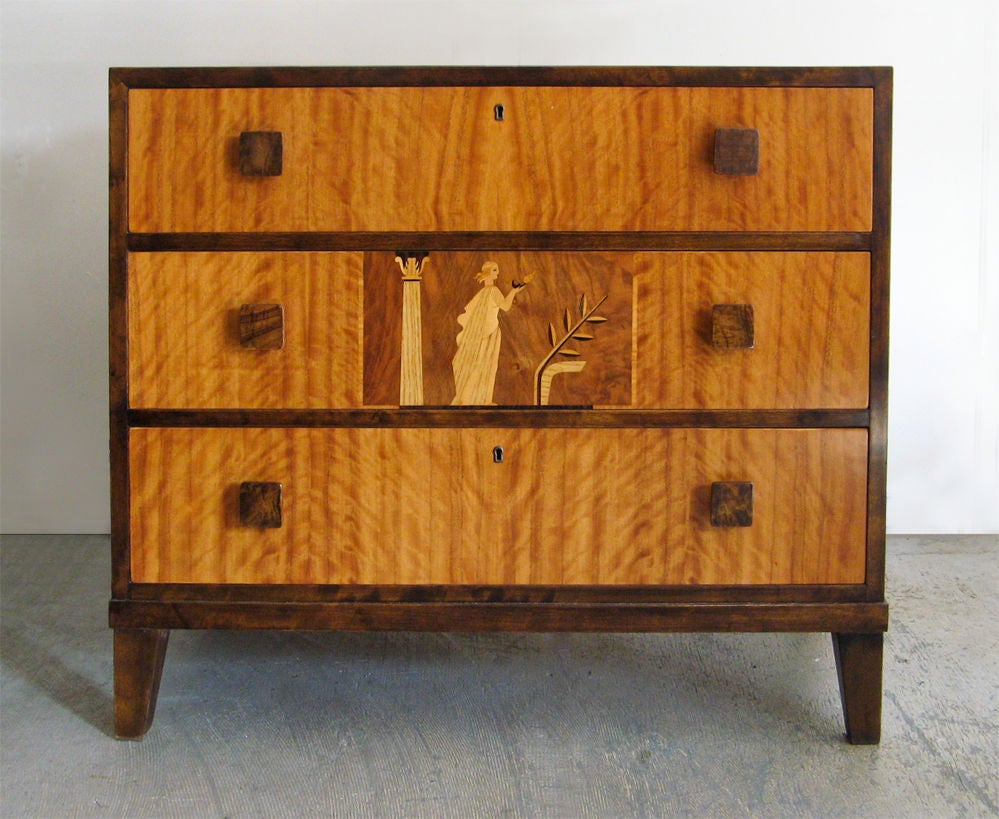 Swedish 1930's Art Deco chest of drawers / nightstand with beautiful marquetry in a variety of exotic wood veneers. The center drawer has a classical figure holding an oil lamp. Dimensions H: 30â?? , Length: 35 1/4