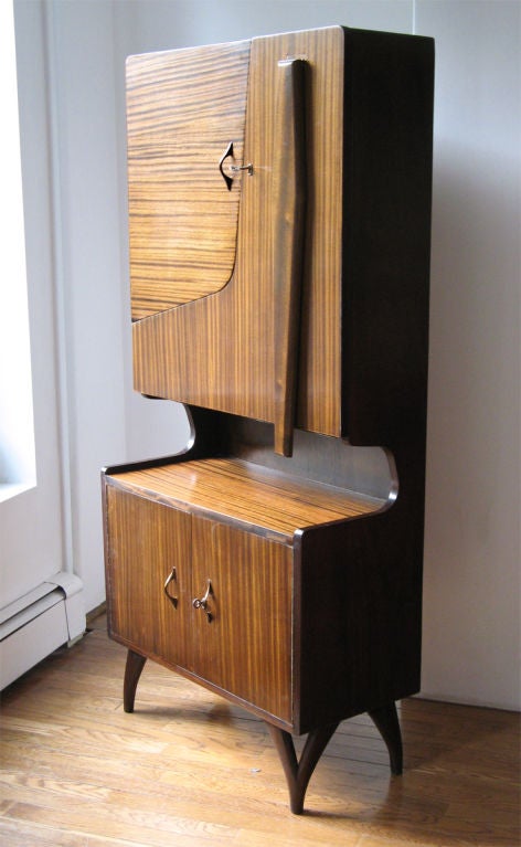 Unique Scandinavian mid-century mahogany bar cabinet with asymmetrical doors. When unlocked the right upper cabinet door drops to create a table surface with original formica. The support leg is held in place with a magnet when in the up position.