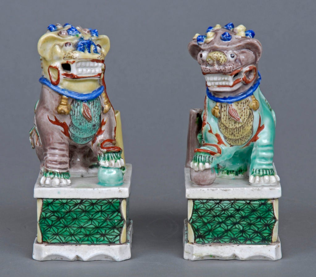 Pair small Chinese porcelain Foo dog incense burners, enameled on the biscuit, both with balls, incense holders and seated on bases decorated with lotus flowers.