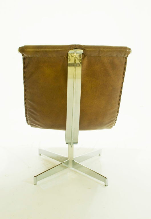 A beautiful saddle-colored leather sling chair supported by a chrome X-shaped base and sloped T-bar. The front and rear panels are stitched together with thick leather lace.