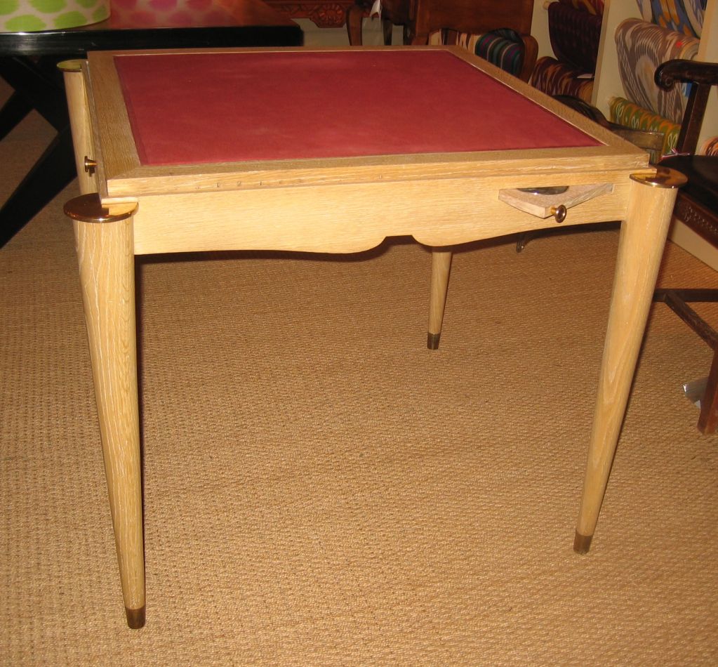A wonderful cerused oak card table with reversable top (red fabric on one side, oak on the other) concealing a storage bin in the interior. The table has a scalloped apron with tapered cylindrical legs and small pull-out ashtray holders on the