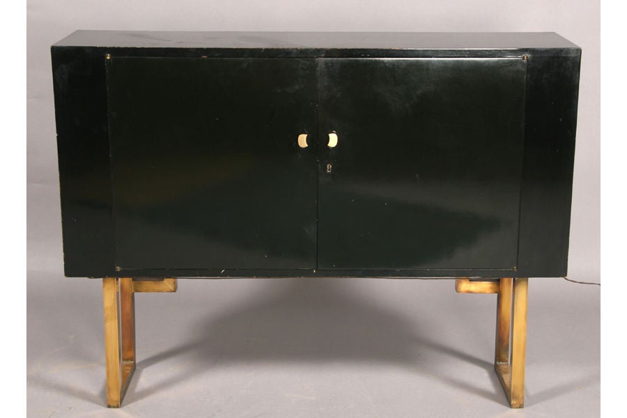 An unusual, small-scale ebonized bar cabinet on gilt brass legs, circa 1930, with cream colored parchment on reverse,the interior fitted for bottles and glasses.