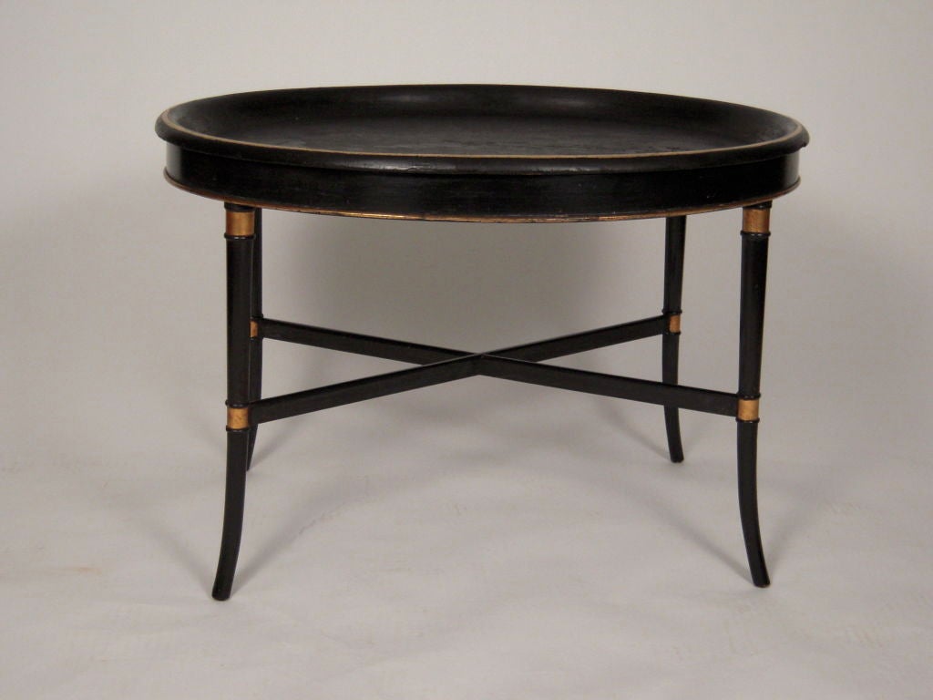 A parcel gilt and ebonized wood coffee table with removable papier mache oval top resting on a wood base with splayed parcel gilt ring-turned legs joined by an X-shaped stretcher.<br />
Good, old leathery surface on removable tray top.  Sturdy.