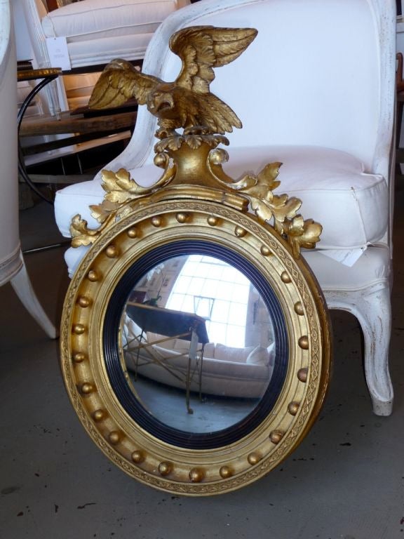 A late 18th Century giltwood convex mirror with carved eagle and foliate crest.