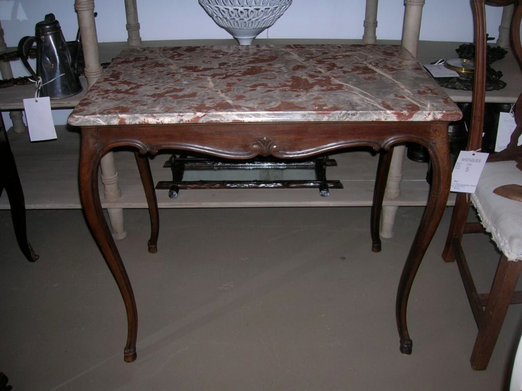 A 19th century, French Louis XV style table with a decorative carved apron, hoof feet and a marble top.