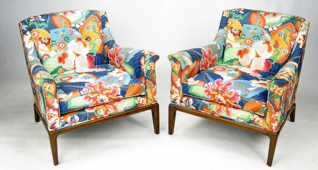 A striking and very well made pair of club chairs in the style of Edward Wormley for Dunbar. The pair is clad in a vibrant floral print chintz with the dominant colors being blue, crimson, and tangerine. The base is a carved walnut with soft