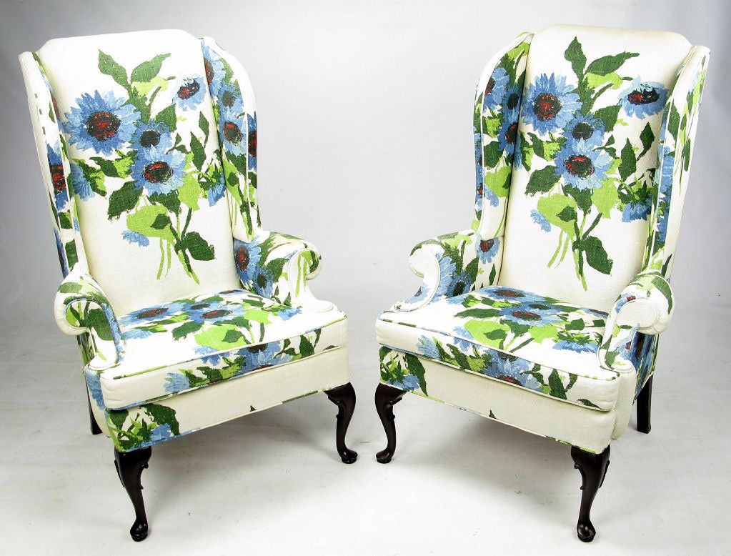 Elegantly modern pair of wingback club chairs from Hickory Chair Company. The over sized floral print linen is comprised of green, blue red and black flowers on a white ground. The front legs are cabriole carved mahogany and the mahogany back legs
