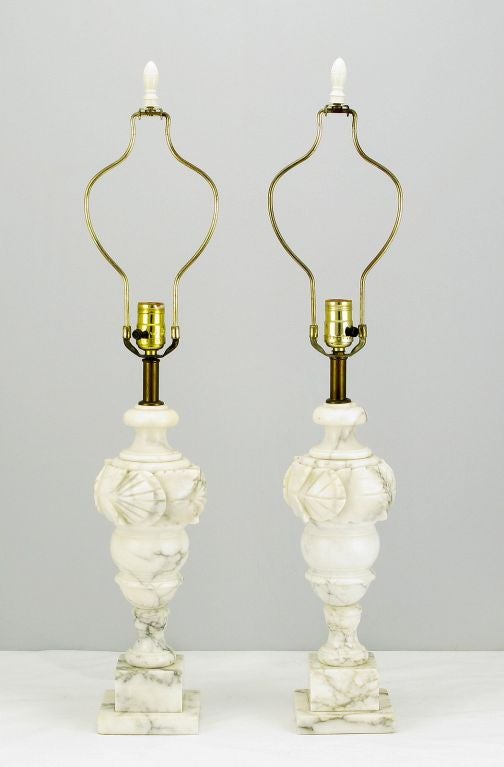 Classic Italian style, these table lamps are hand carved of Italian Carrara marble. The plinth block two part base supports the vase form body with carved shell motif. Perfect size for the mantel or the vanity. Stamped Italian Import. Sold sans