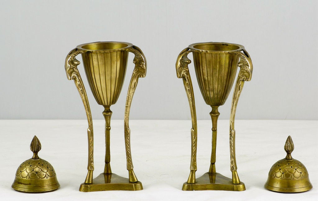 Beautifully patinated Empire styled brass incense burners adorned with three rams heads and hooved pilaster legs surmounted on trefoil brass bases. The pierced cap has a flame finial top and is removable. The conical incised center urn has a bottom
