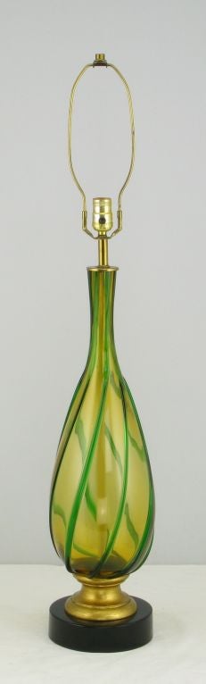 Beautiful amber and green Murano glass bodied table lamp. The vase form body is mounted on a gilt wood and black lacquered  metal base. Sold sans shade.