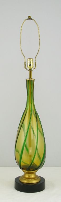 Belle lampe de table à corps en verre de Murano de couleur ambre et verte. Le corps en forme de vase est monté sur un support en bois doré et laqué noir  base métallique. Vendu sans store.