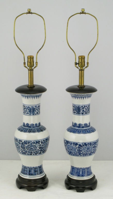 Excellent pair of Chinoiserie blue and white glazed ceramic table lamps. The blue chrysanthemum design and traditional Asian patterns are very crisp. The cap and base are black lacquered wood. Sold sans shades.