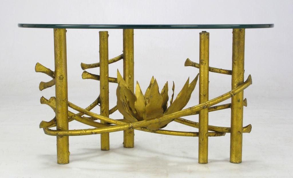 Wonderfully preserved petite coffee table, featuring heavy iron base supports and original glass top. Has a total of six legs, with sinuous iron stretchers that support the asymmetrical placement of a metal lotus flower.