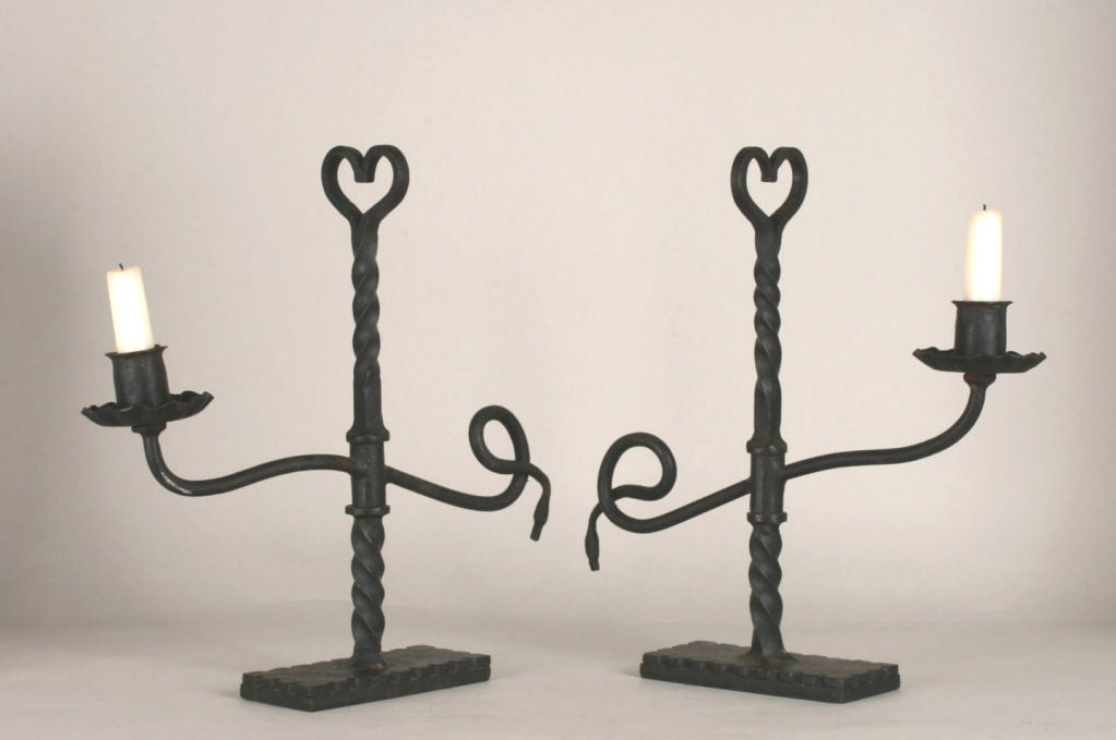 Fine pair of heavy wrought-iron swivel candlesticks. Twisted upright stem, culminating in an open-work heart and with an attached swiveling cross arm with the candle cup on one end and counter-balanced with a swan head.<br />
<br />
Completely