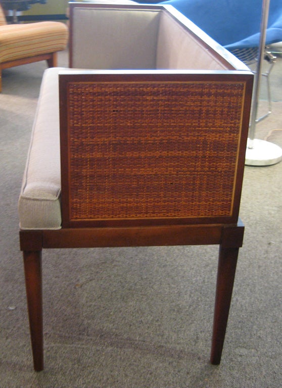 Small upholstered bench of solid walnut with cane arms and seat and seat back upholstered in fabric on frame of solid walnut