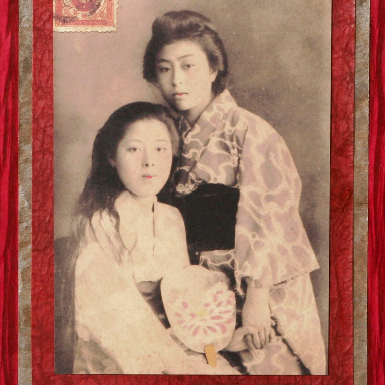 Vintage print of two young Japanese women in traditional kimono. Historic Japanese postage stamp affixed to upper left hand corner of image. Photograph is backed with many layers of textural rice papers in shades of red, burgundy, magenta and wheat.