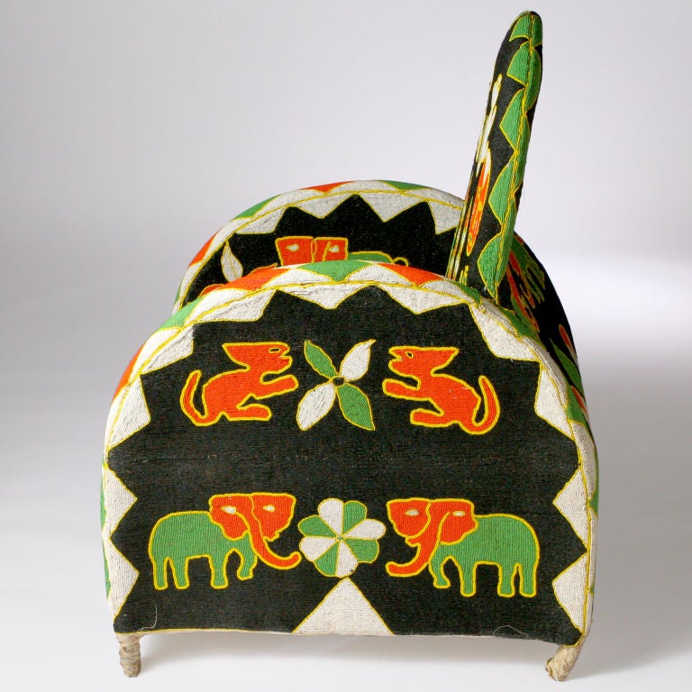 Exquisitely crafted Nigerian chair in vivid colors with dramatic black background. Hand-upholstered beads create a vibrant pattern depicting African animals juxtaposed with geometric shapes.