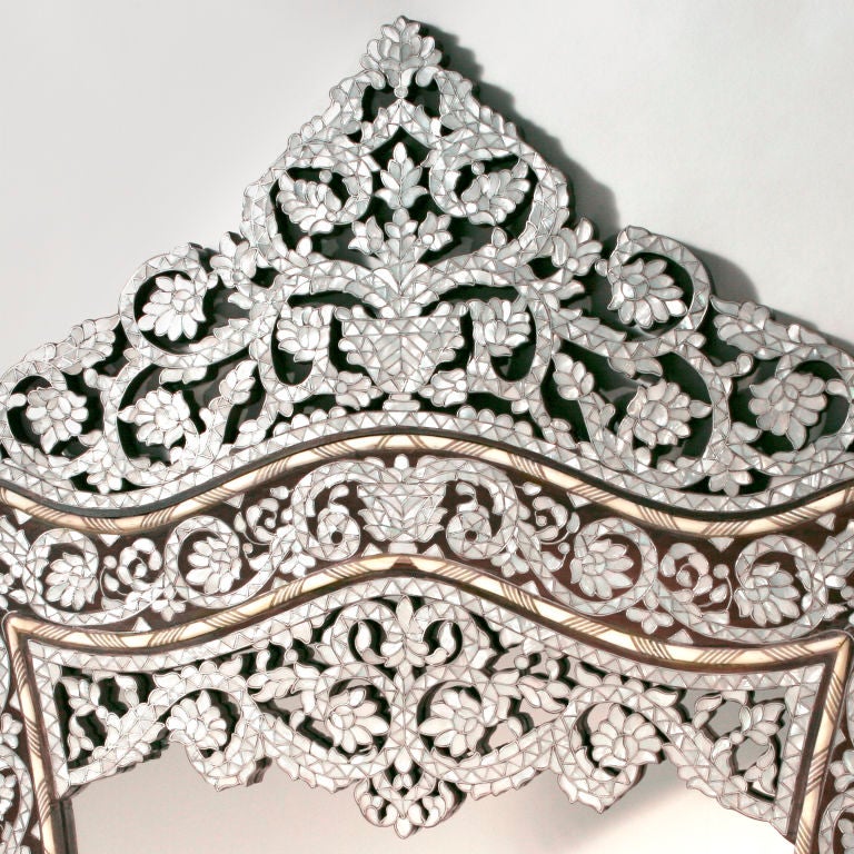 Hand-carved Syrian walnut mirror in a delicate bombe shape with swirled mother-of-pearl and camel bone inlay. Intricate accents festoon the corners of the piece, while the elaborately carved crown curves upwards in undulating patterns.  Our design;