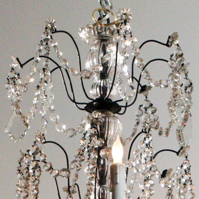 Italian eight-light chandelier festooned with beaded roping; a central glass baluster column surmounted with a crown of cut crystals and branches heavily ornamented with long tear drop pendants.