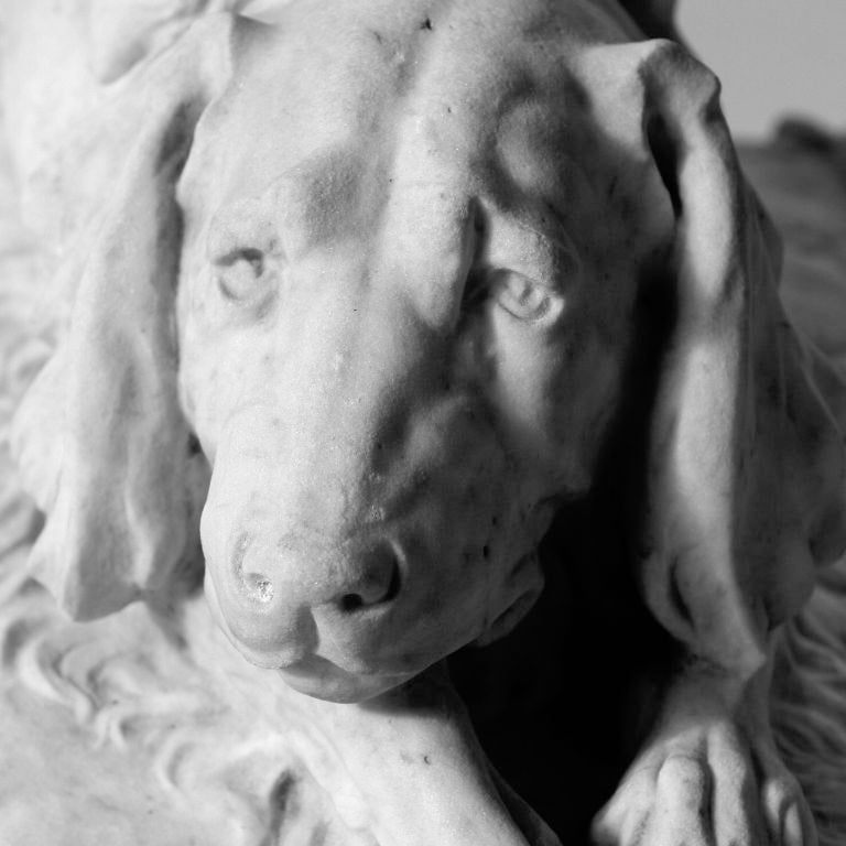 Life-sized carved white marble sculpture of a spaniel on tufted cushion with tassels. A rare estate piece!