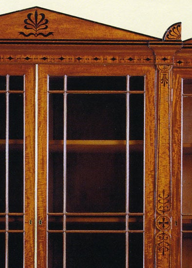 Regency neo-classical ebony-inlaid mahogany breakfront bookcase in the Grecian style after a design by George Oakley. The <br />
pediment centering anthemion decoration over glazed doors flanked by anthemia decorated stiles; the base with