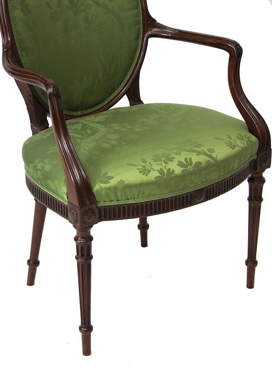 A George III mahogany oval-backed upholstered open armchair in the Hepplewhite taste.