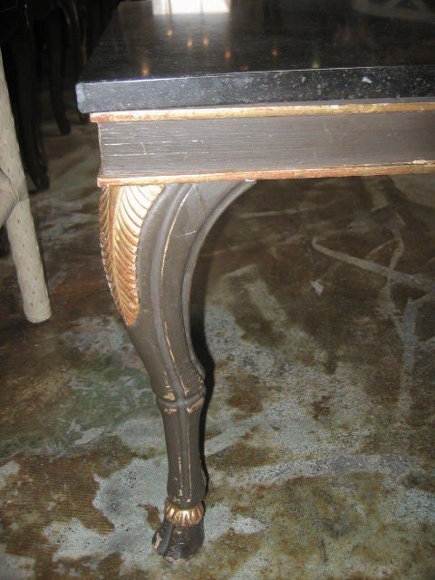 Beautifully hand carved table with dark brown-green paint finish. Gilt detailing on the goat legs and hoof feet. The knees are decorated with a carved and gilded palm frond. The marble top is a dark brown-black color.