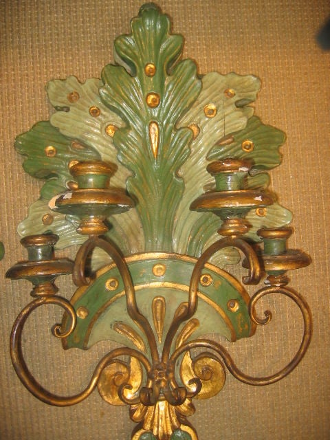 Solid, wood carved wall sconces with original paint and gilt finish. Each sconce has four metal scrolling arms which support a single candleholder. The carved motif is of a fan of 14 double layered acanthus leaves in alternating colors of green with