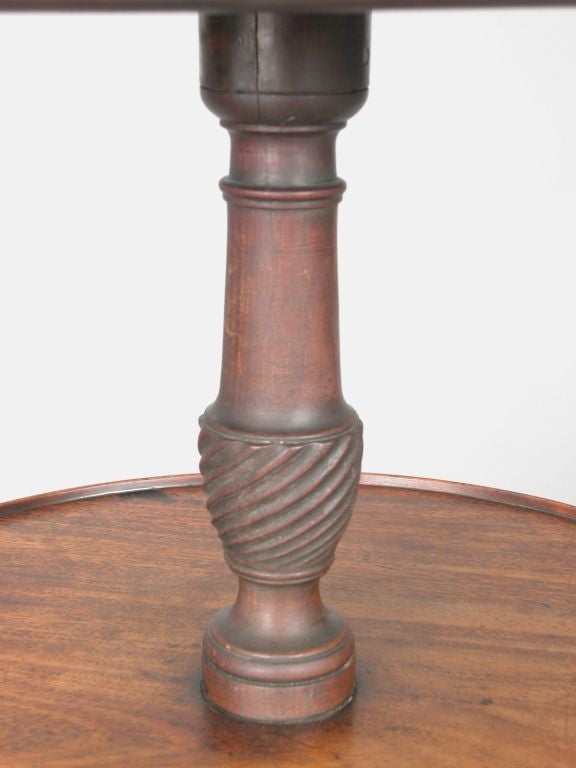 An unusual 18th century English mahogany four tiered dumbwaiter in old surface.  Each turned and dished shelf is supported by a spiral carved urn standard on a tripod cabriole base ending in pointed slipper feet.  A later additional book paneled