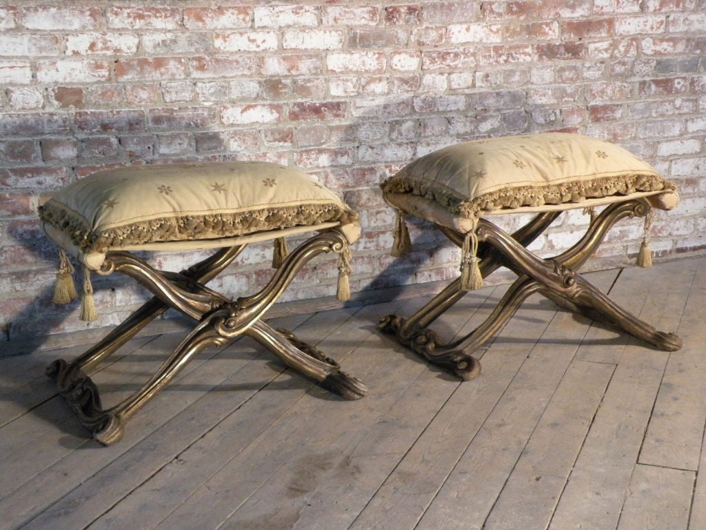 Les bancs pliants ont des bases en bois sculpté et doré en forme de X, des dessus et des coussins en tissu. 
