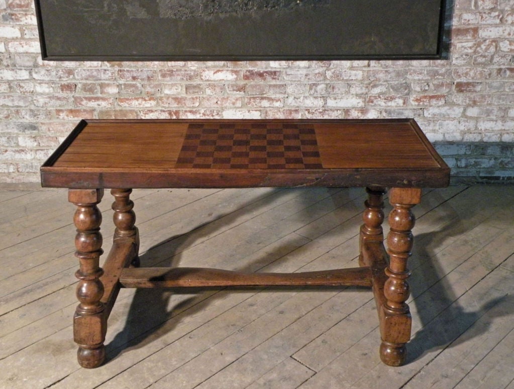 Unique low table, the framed rectangular top inlaid to function as a game board. One concealed drawer at the end to hold the game pieces. The boldly turned legs joined by H-stretcher.
