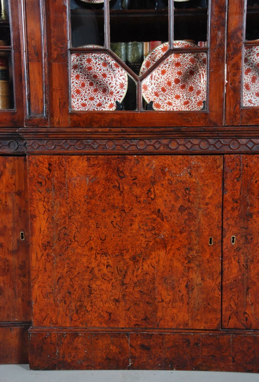 A 15 1/2' long bookcase of double-breakfronted form. Rare for the use of exceedingly figured yew wood veneers throughout. The astragals of the 12-pane glazed doors are fashioned out of solid yew. With an outswept cornice featuring a strip of
