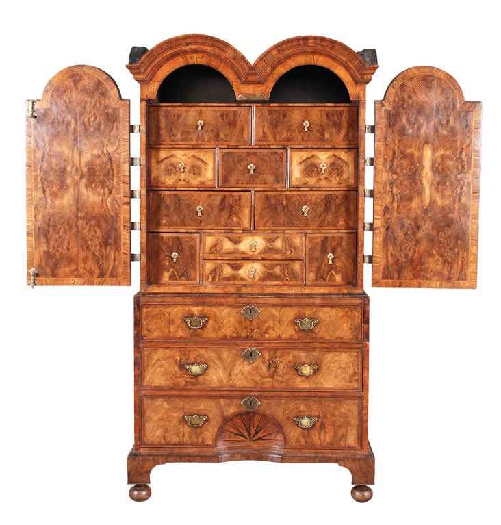 A Queen Anne period double dome cabinet veneered in walnut and burl walnut. The quarter-veneered doors are mounted with etched and pierced brass strap hinges. Behind the doors is a fitted interior of walnut veneered drawers. The base consists of