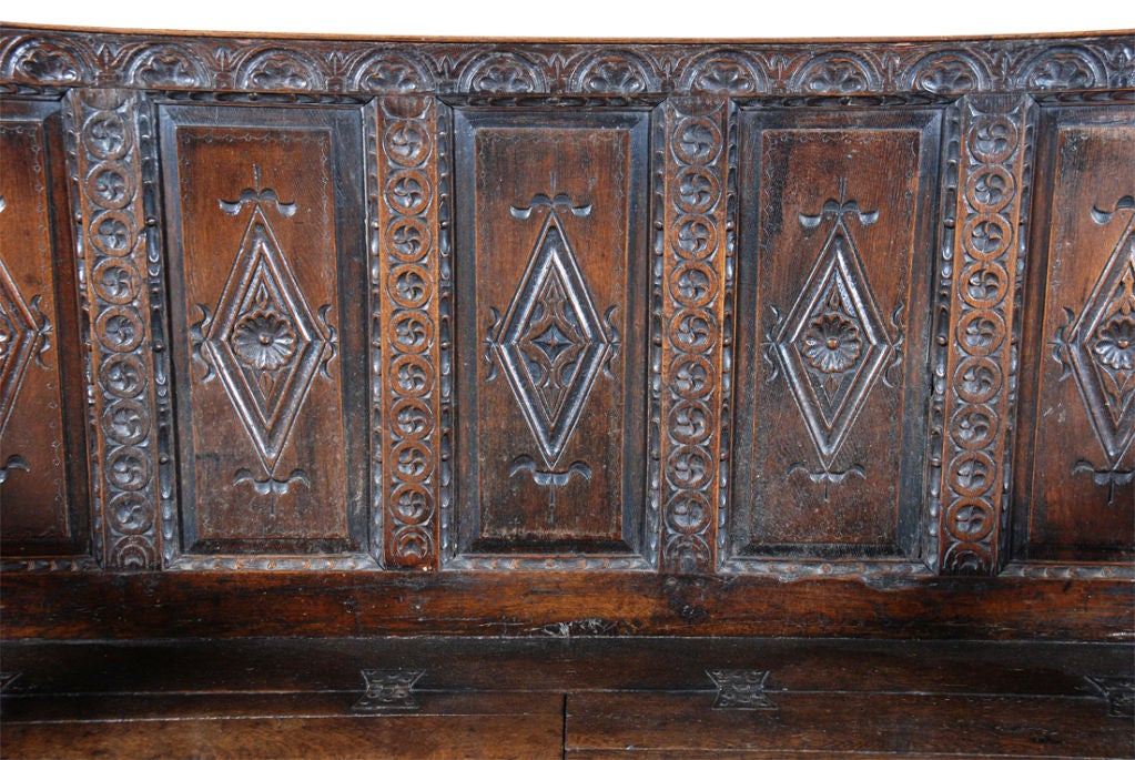 A Charles II period oak settle with a raised-paneled back. Each panel is carved with lozenges centered by florettes. With thick, shaped arms on turned supports. The cupboard base is also paneled and the seat consists of two separate hinged lids