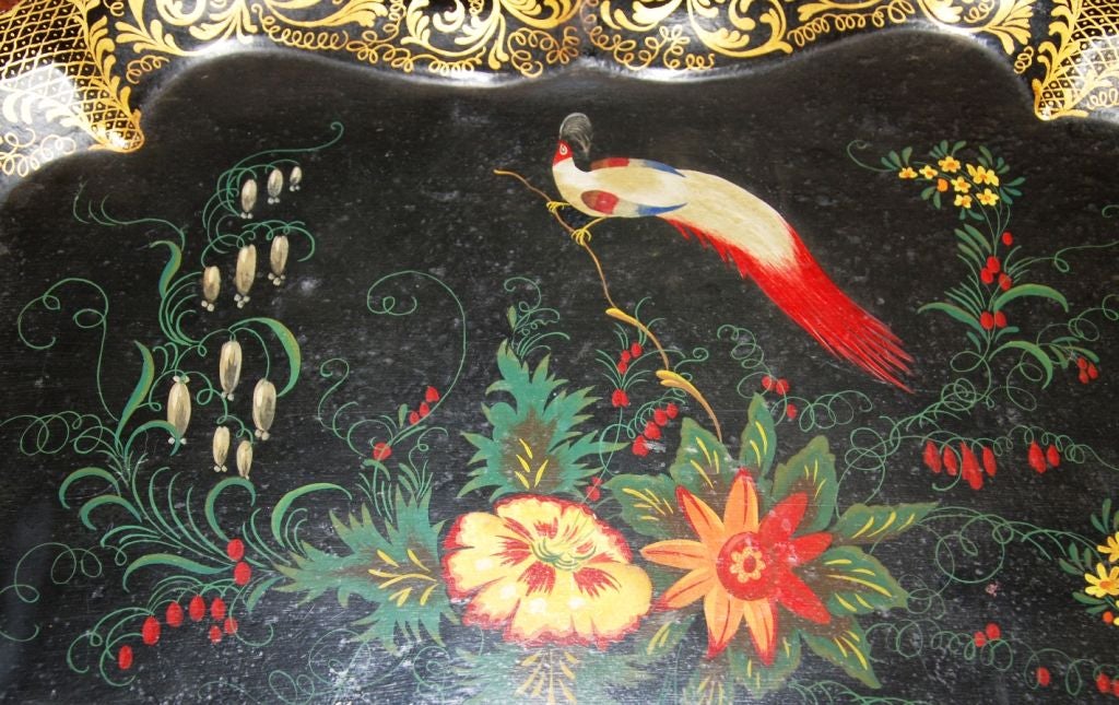 An elaborately decorated tole tray with a hand painted floral and bird motif as a central design on a black painted ground. There is a scalloped edge which has hand painted detailed scrollwork in gold leaf. It is a Victorian English tray from the