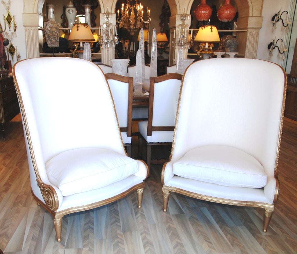 A pair of extremely dramatic and large scaled Art Deco style upholstered chairs with gilt wood trim. Styled after the 'Fauteuil Nautile' chair by Paul Iribe from 1913. They have a striking carved shell shaped decoration at the base of  curved arms