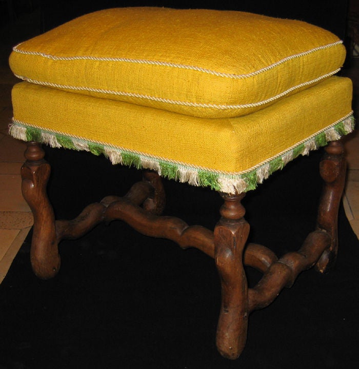 A walnut stool with ‘Os de mouton’ legs and stretcher, yellow upholstered seat cushion, with green and cream fringe.