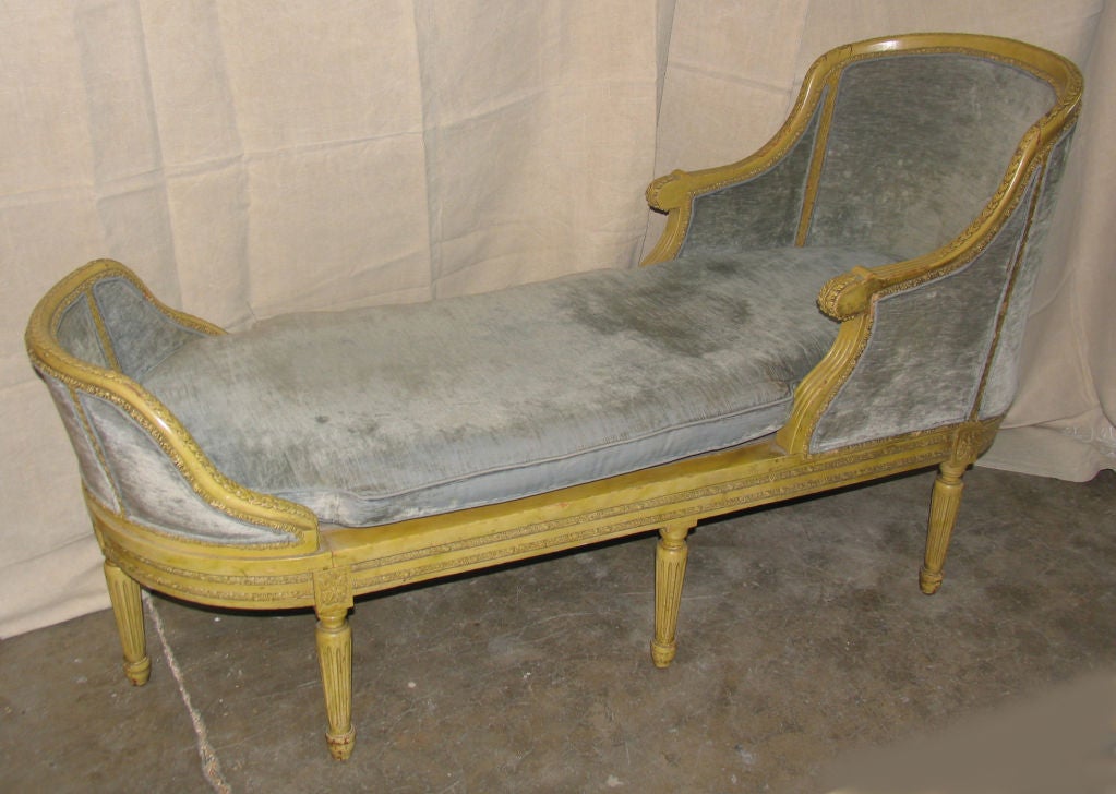 Handcarved Painted and upholstered chaise lounge in Louis XVI style with curved back and foot featuring acanthus leaf and floral carved borders all raised on seven fluted legs