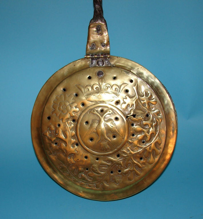 A Continental early 18th century pierced brass bed warmer with a forged iron handle, the pan decorated with a crowned two-headed eagle.