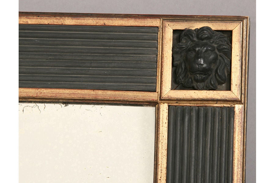 Regency style mirror with a reeded frame, gilt banding , and lion's head detail on the corners.