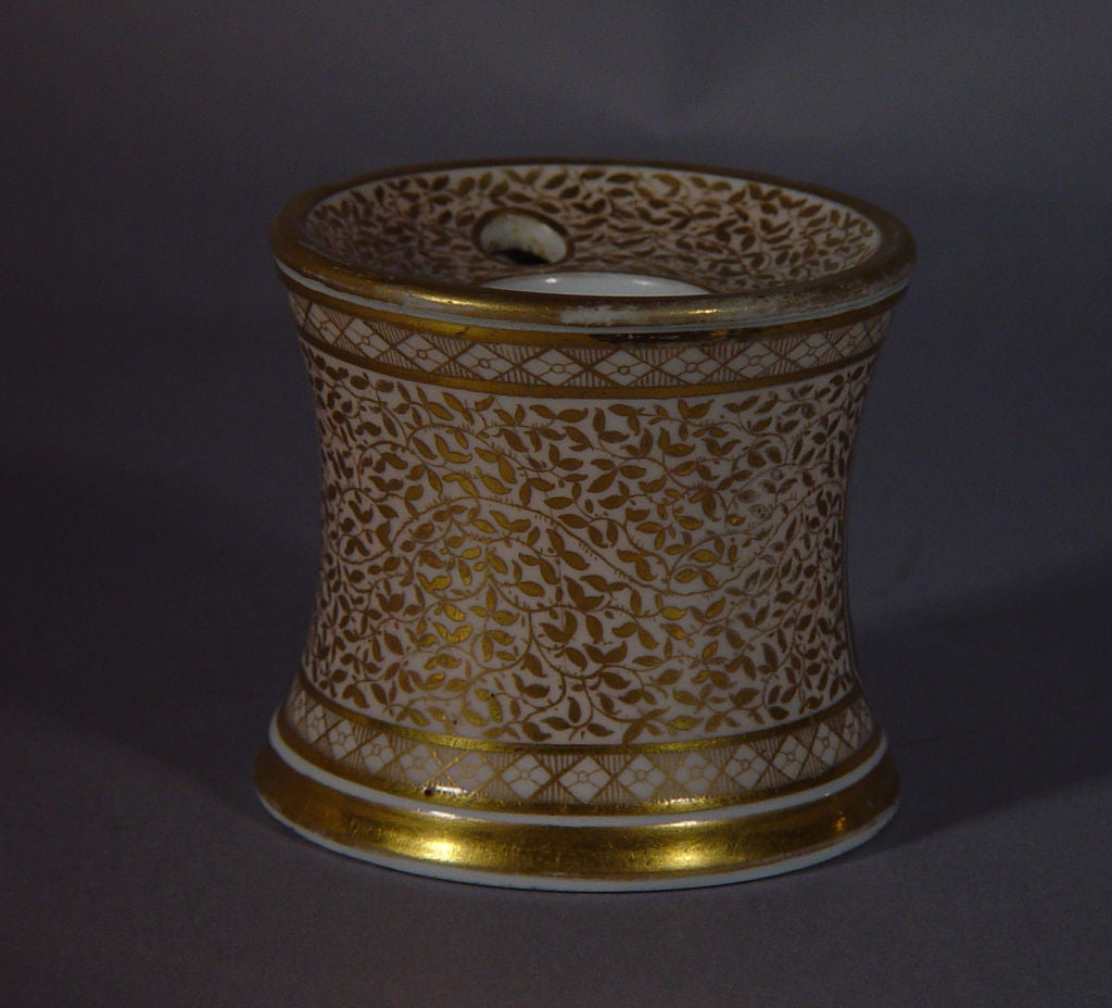 The cylindrical form inkwell has concave sides and top. It is beautifully painted with a panel of feather decoration within a wide gilt border with a gilded leaf decoration over a delicate light peach ground with neoclassical diamond bands above and
