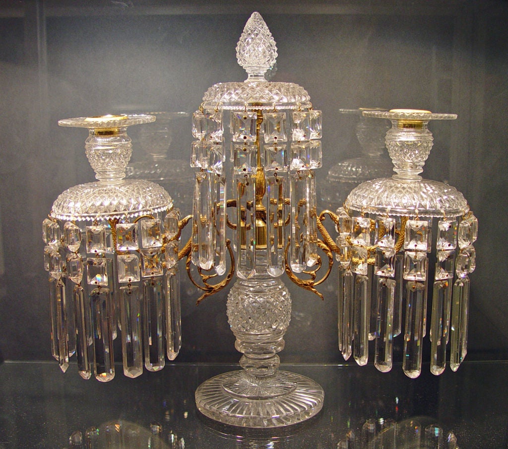 The candelabra sits on a circular foot with a central glass stem mounted by two branches.  The top of the arm rises to a concave glass canopy with drops suspended below and a flower-head shaped finial.<br />
<br />
Each arm has a matching canopy