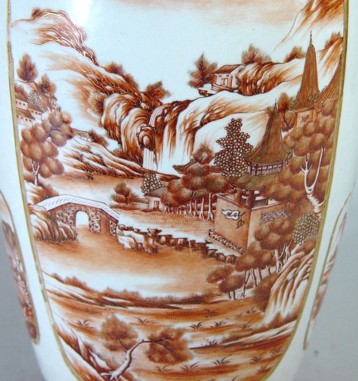 The vase well painted in sepia with landscape panels to both sides.  To each side are smaller landscape panels within raised gilt borders.  Around the neck are ruyi-head collars. The finials are in the form of seated lady holding a cup beside garden