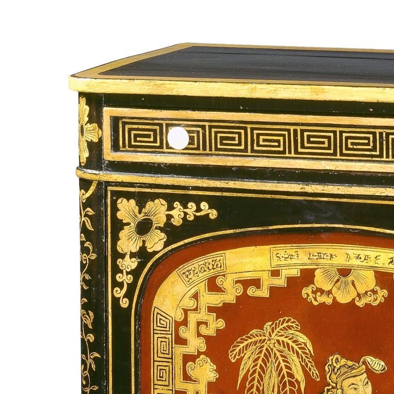 A Regency Japanned side cabinet, the rounded edge top with a painted gold border, above one long drawer with ivory handles and painted Greek key motif decoration, fitted with fifteen small compartments, above a cupboard door inset with an arched