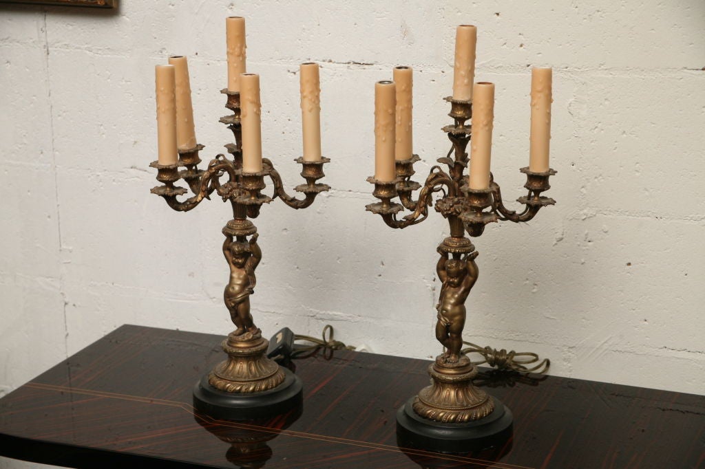 Estate items from Former Mayor of Palm Beach Claude Dimick Reese. A stunning pair of late 19th century bronze 5 light lamps/ candelabra in the form of nude cherubs, each holding up a basket of overflowing fruit and five foliate branch arms with 5