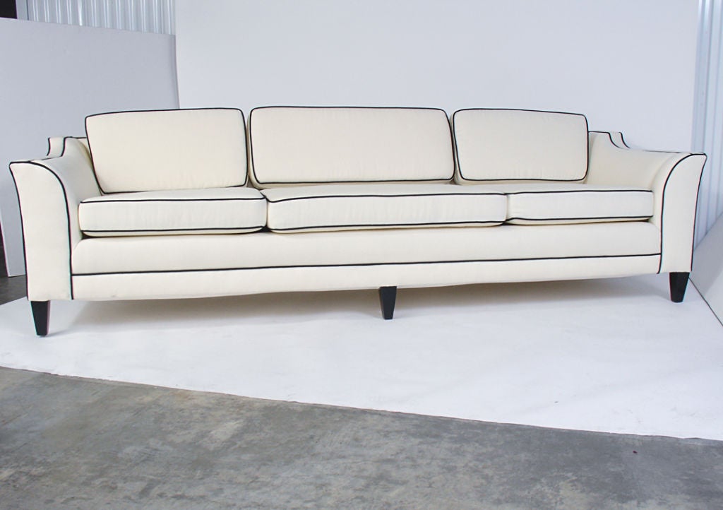 Glamorous Art Deco Sofa, American, circa 1940's. Sexy Art Deco lines, and extremely comfortable. Reupholstered in an ivory linen upholstery with contrasting black piping and black lacquered legs.